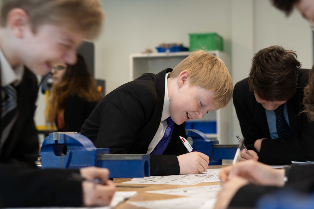 Three Leigh UTC students are shown sitting together at a desk and laughing, whilst working on their work.