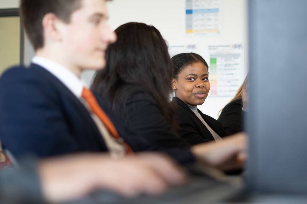 A small group of Leigh UTC students are shown sitting at desks with computers and conversing with one another.