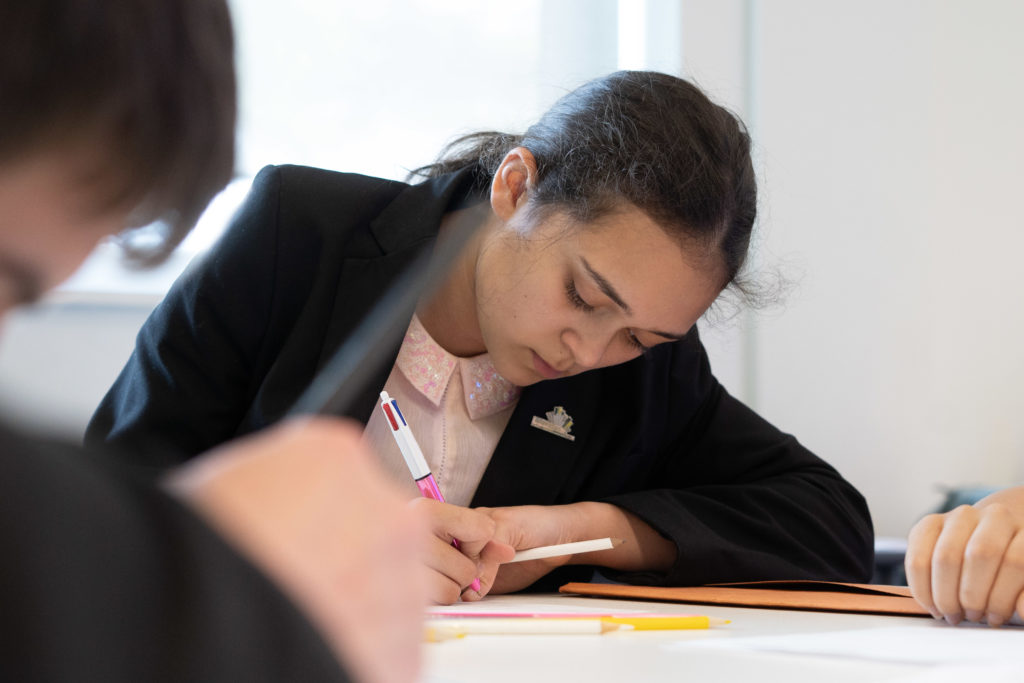 A Leigh UTC student is shown sitting at a desk, working with a pen in her hand.