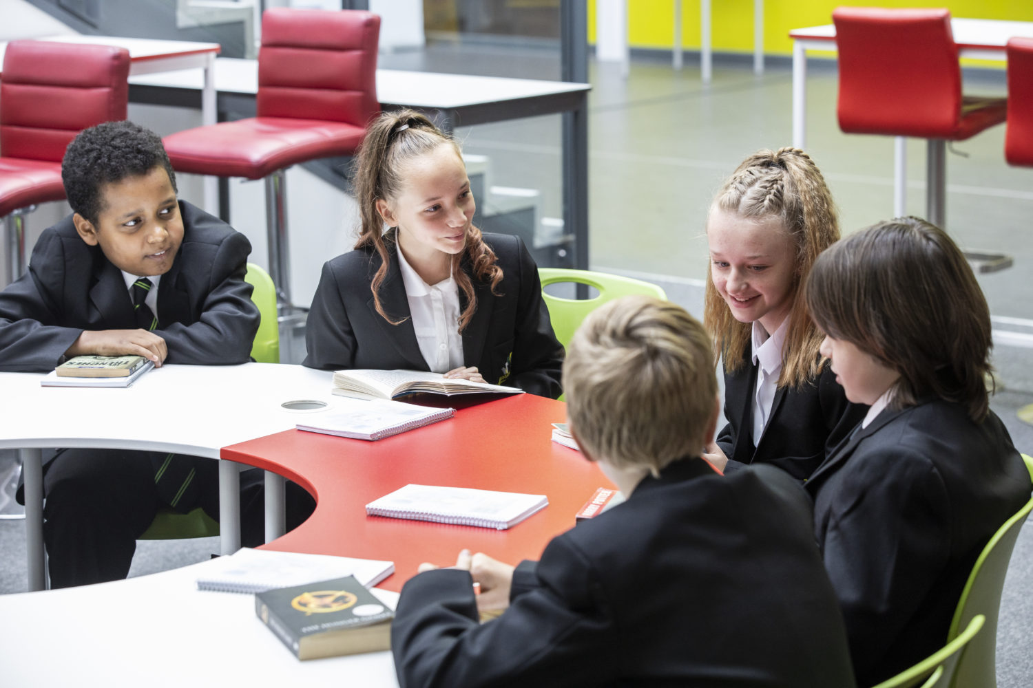 Five students around a table, having a discussion, with notepads and books in front of them