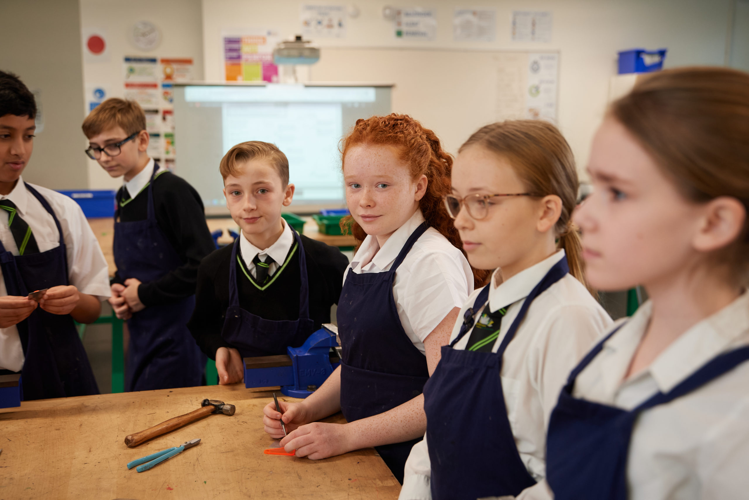 Six Inspiration Academy students, three boys and three girls, are pictured standing around a worktable, wearing aprons, during a DT class.