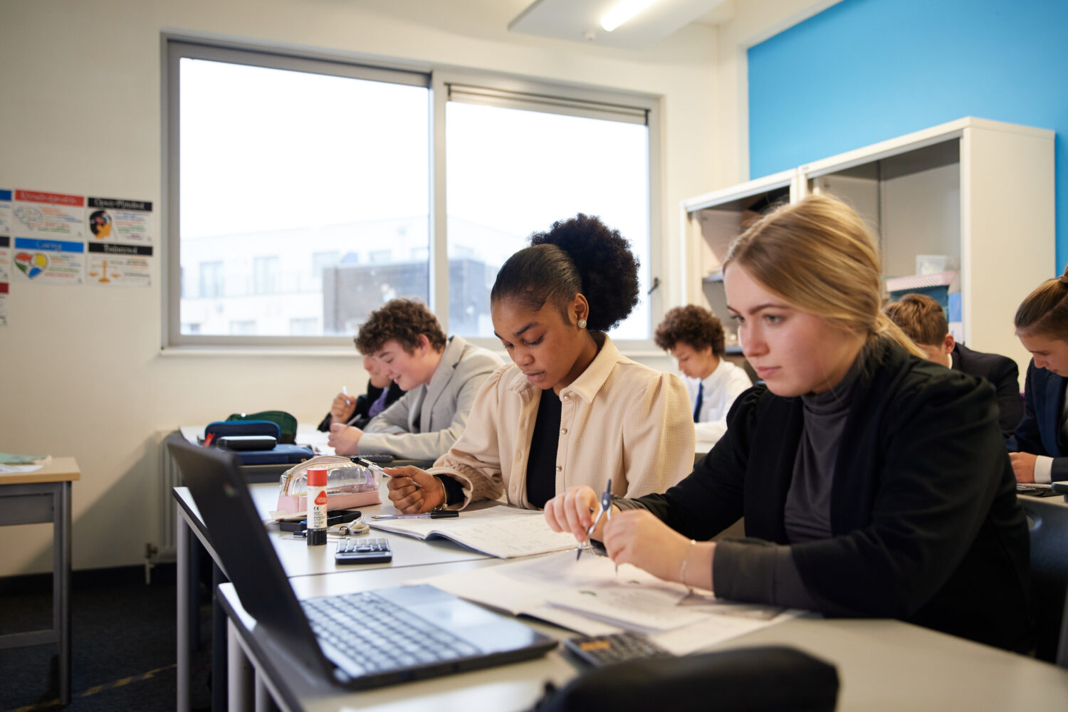 A small class of Post-16 students can be seen sat at their desks, focusing on their work. One student is using a Chromebook laptop to assist her with her learning.