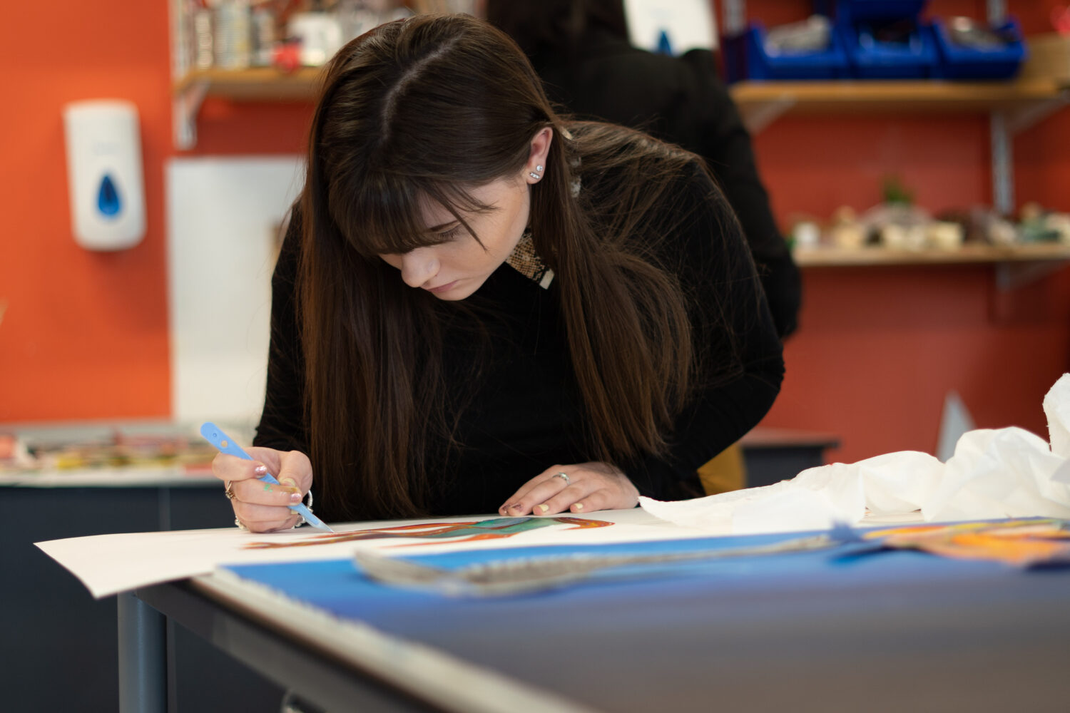 A female Post-16 student is pictured concentrating closely on some artwork she is working on inside an Art Studio.