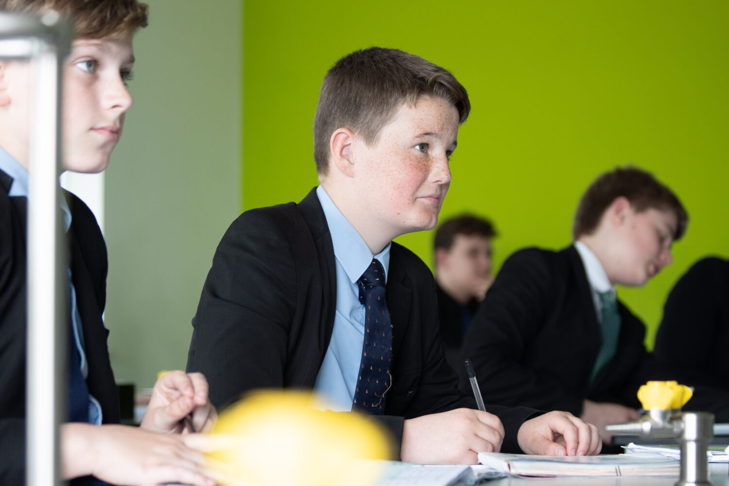 Four male students are shown sitting at their desks in a Science lab with their eyes towards the front of the room.