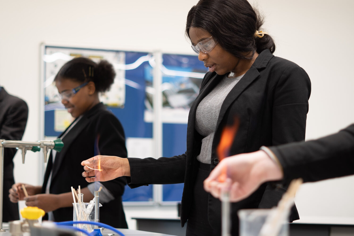 Two female Post-16 students can be seen burning pieces of Magnesium in a Science lab, whilst wearing safety goggles.