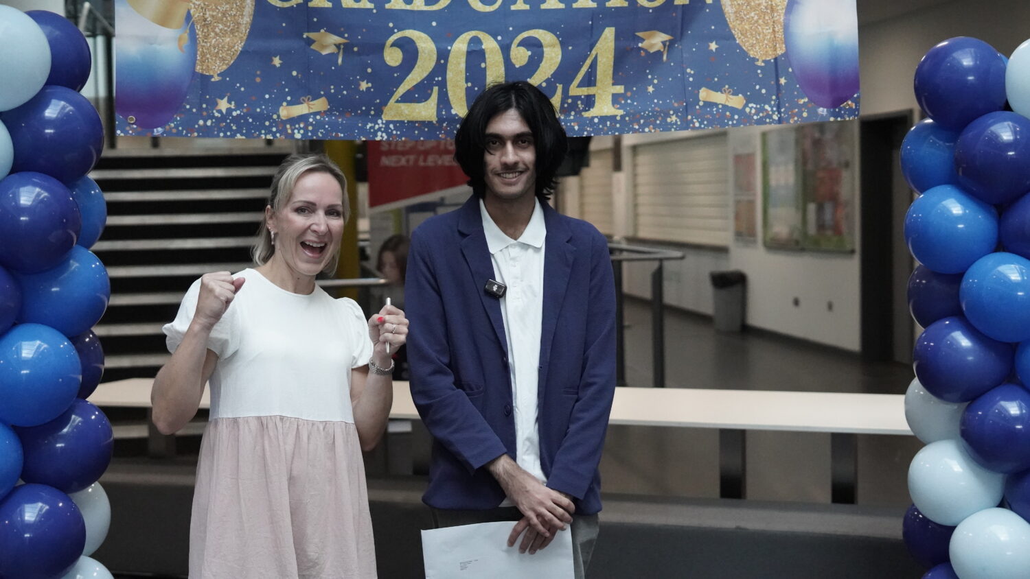 A male Post-16 student is pictured smiling for the camera alongside a member of staff, after having just opened his A-Level results.