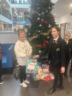 a young school girl with a woman posing in front of a christmas tree with gifts underneath